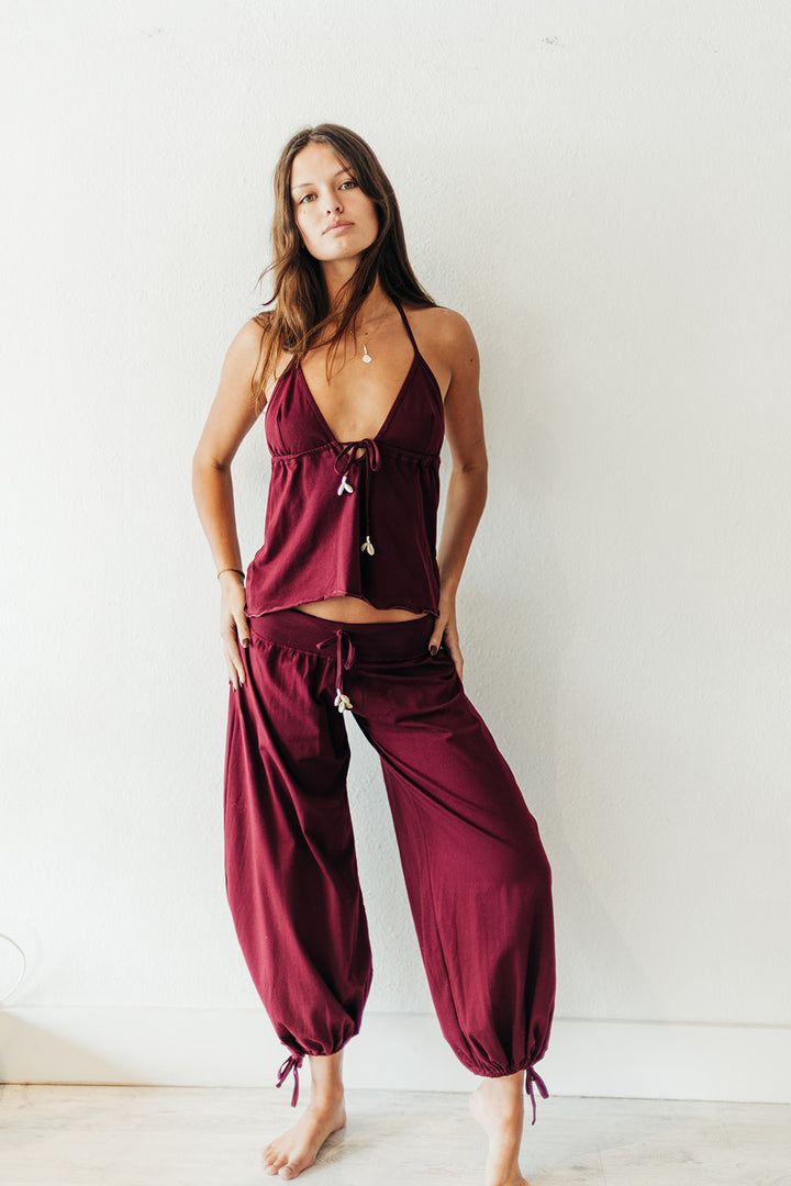 Woman wearing a burgundy pant  top against a white wall