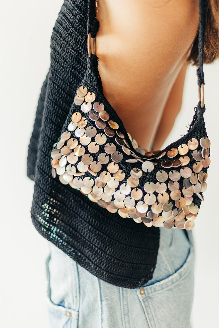 Black handbag with gold sequins held by a person wearing a black sweater and light blue jeans.