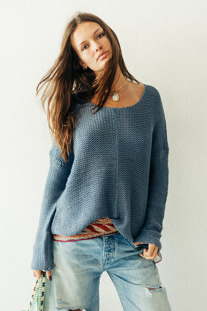 Woman wearing a blue knitted sweater and jeans against a plain background