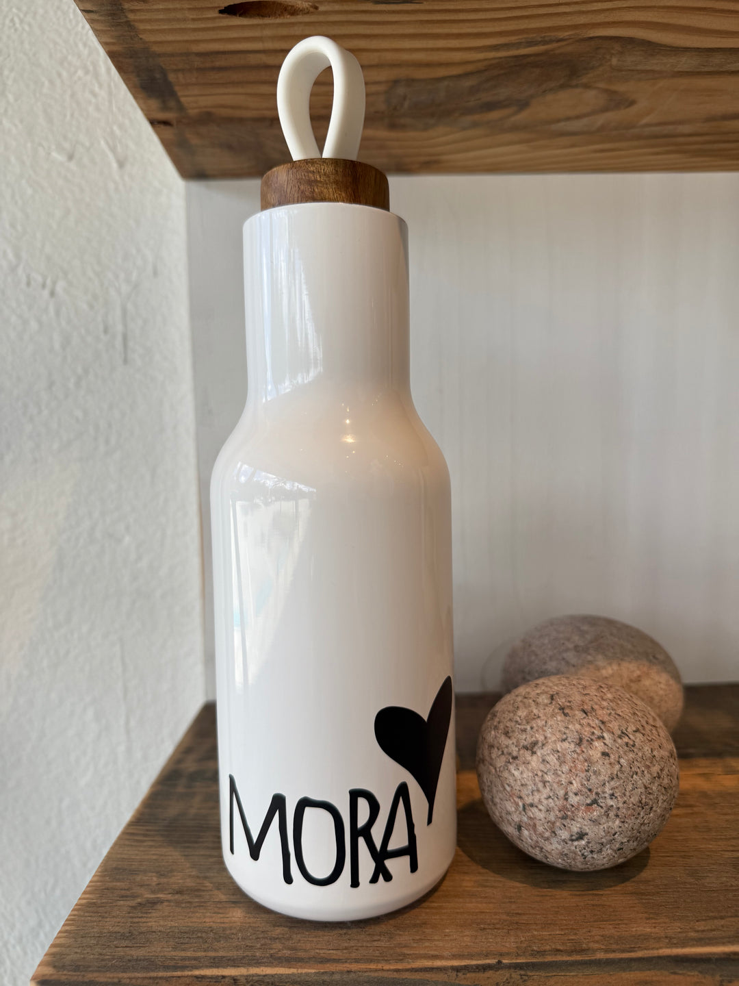 White bottle with 'MORA' and a heart design on a wooden surface
