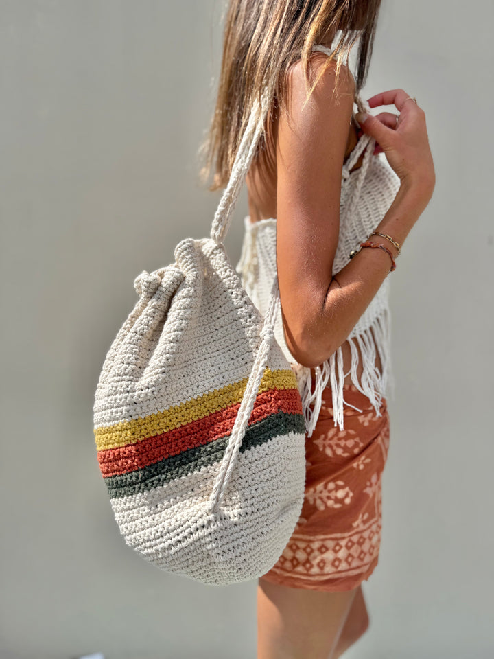 Person holding a crocheted bag with colorful stripes against a plain background