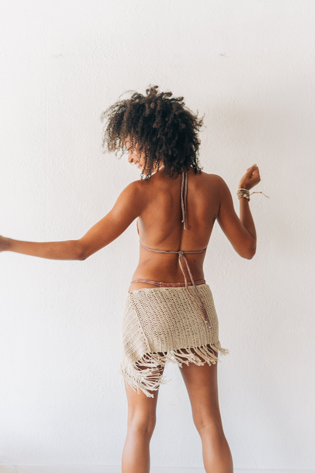 Woman wearing a strappy top and fringed skirt against a white background