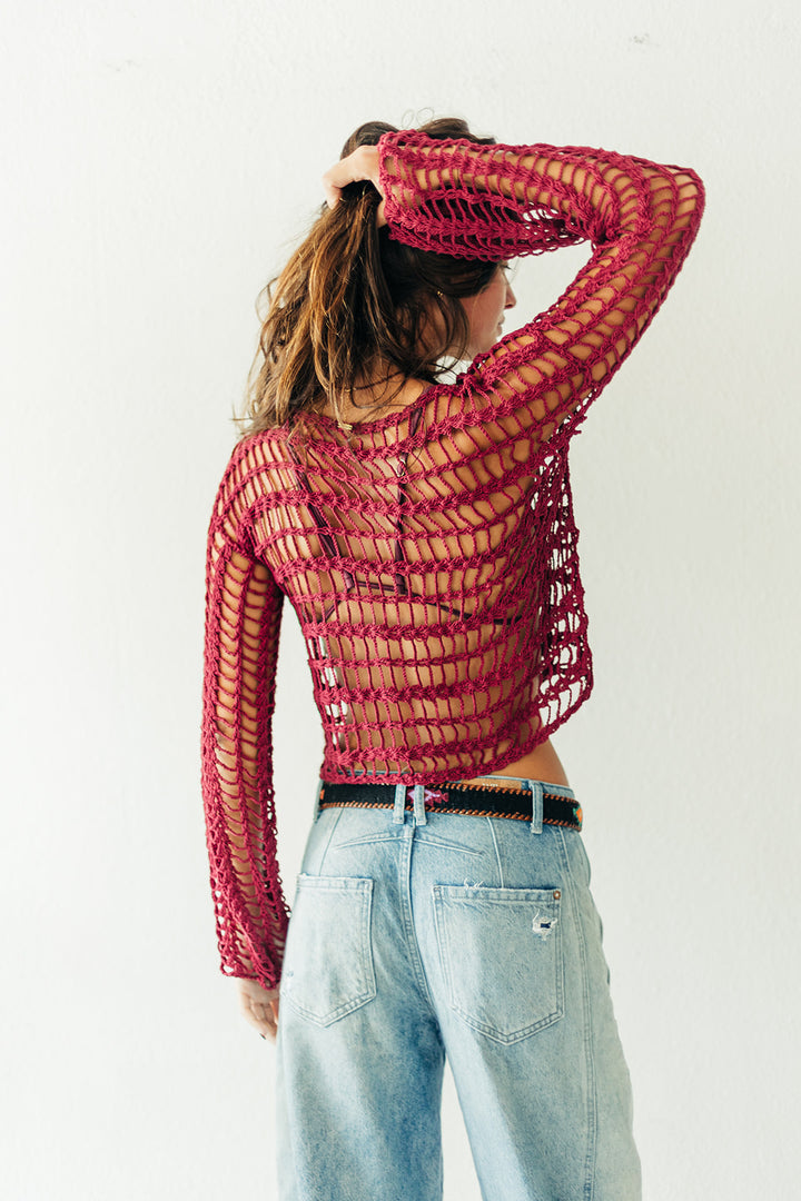 Person wearing a red mesh top and light blue jeans against a white background