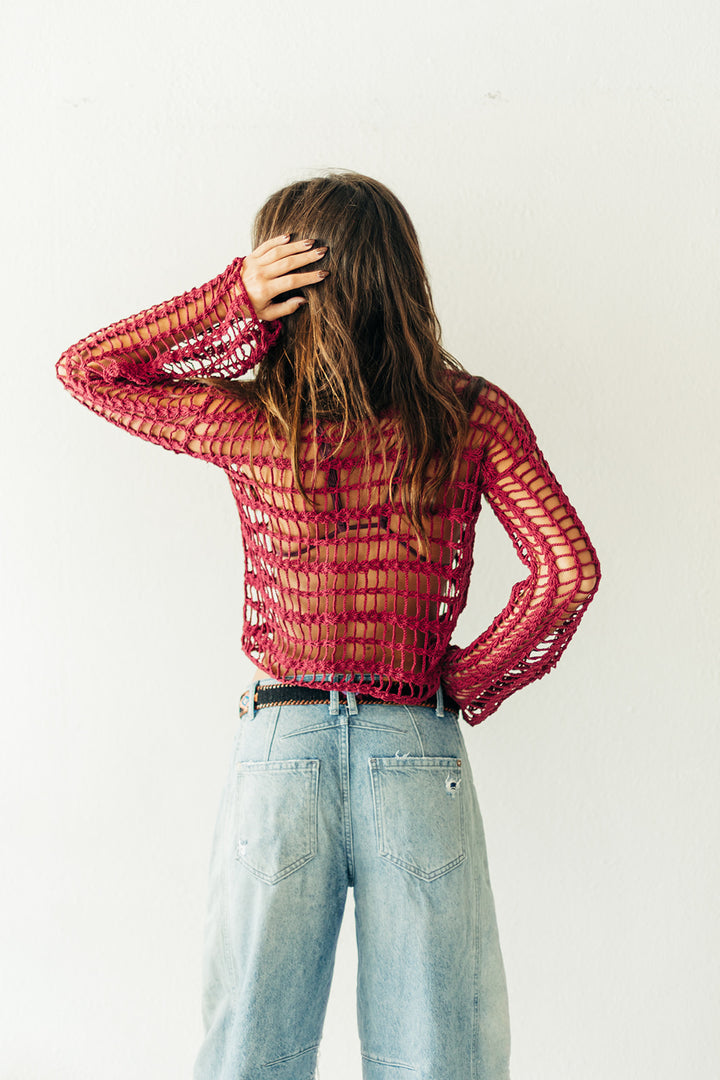 Person wearing a red mesh top and light blue jeans against a white background