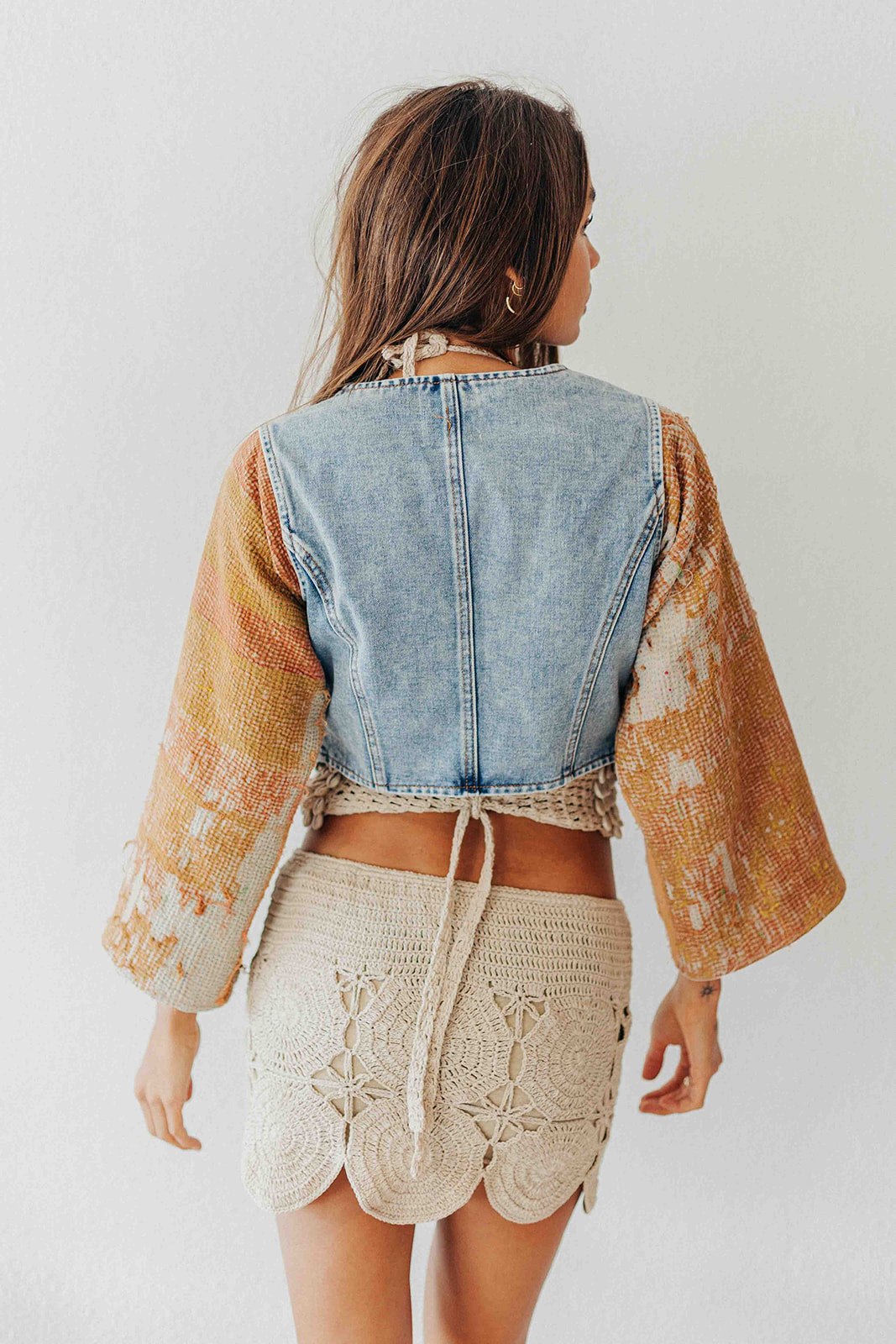 Person wearing a denim vest over a patterned top with beige shorts on a white background