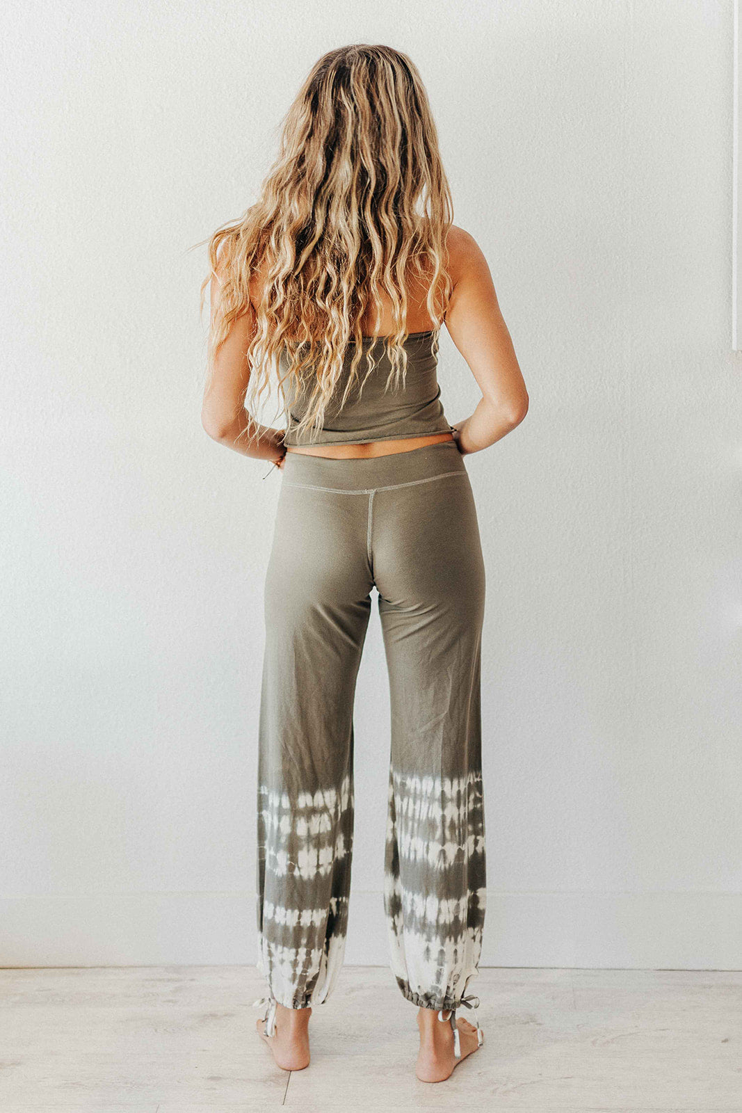 Woman wearing a green tank top and tie-dye pants against a white background
