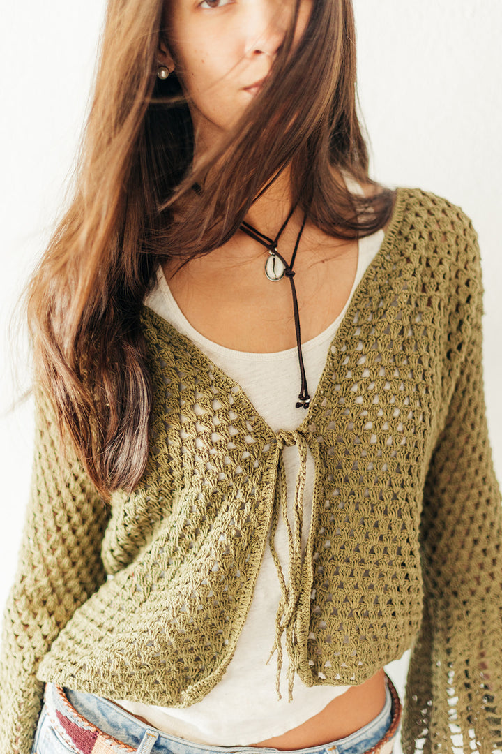 Woman wearing a green crochet cardigan over a white top with a plain background
