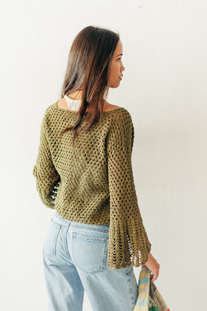 Woman wearing a green knitted sweater and light blue jeans against a white background