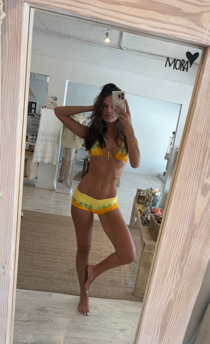 Person taking a mirror selfie wearing a yellow bikini in a room with wooden flooring and furniture.