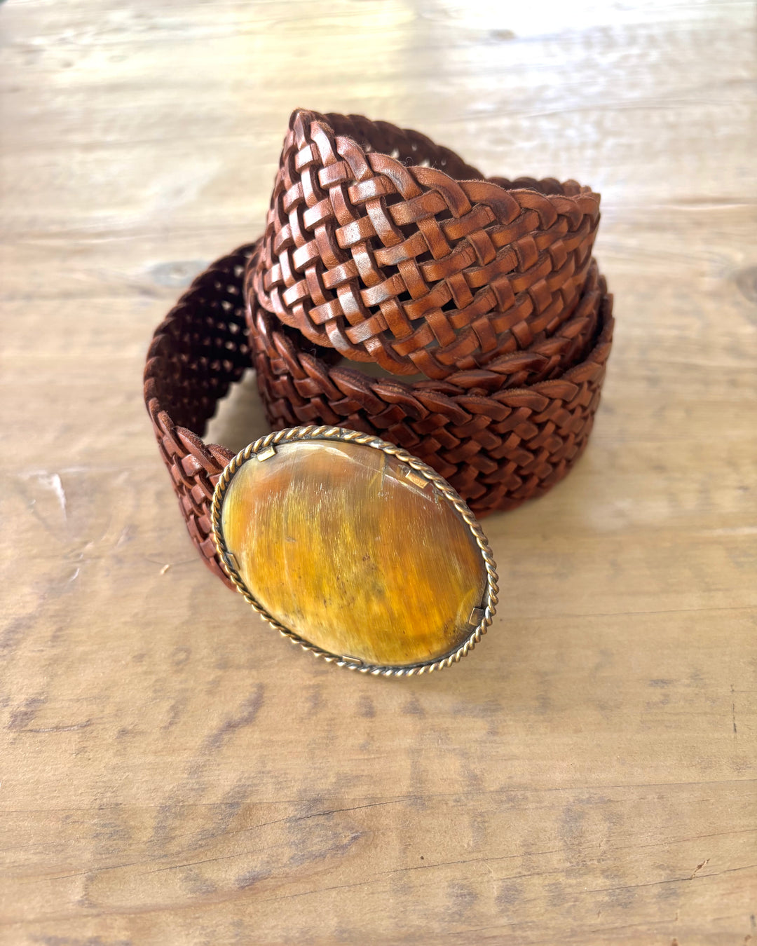 Brown woven belt with a large yellow stone buckle on a wooden surface