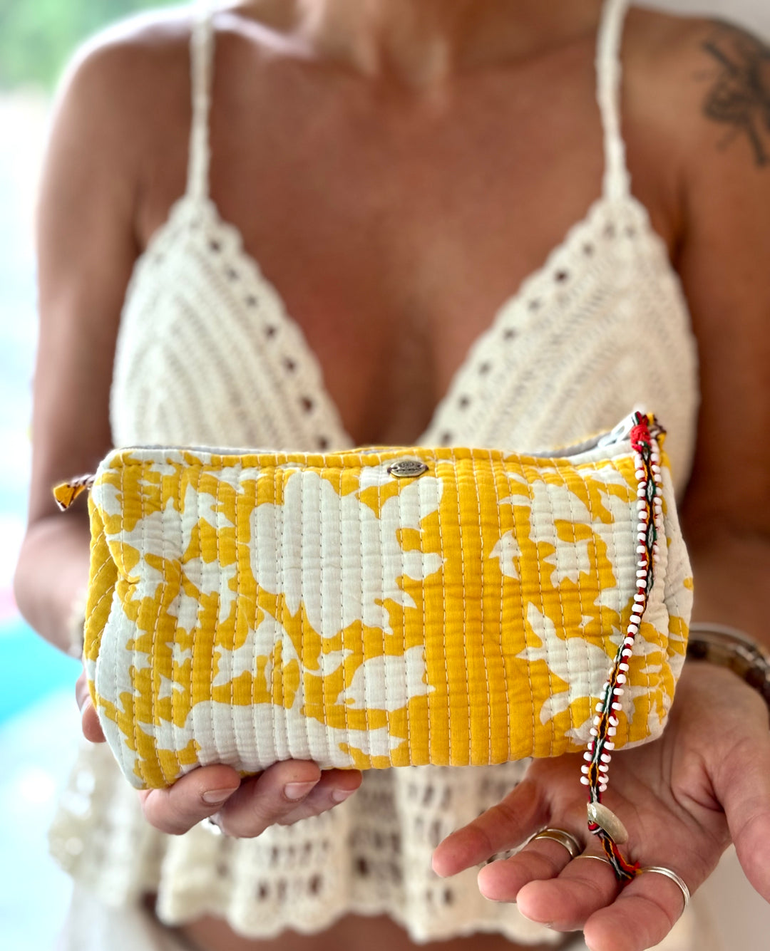 Person holding a yellow and white floral clutch with a blurred background