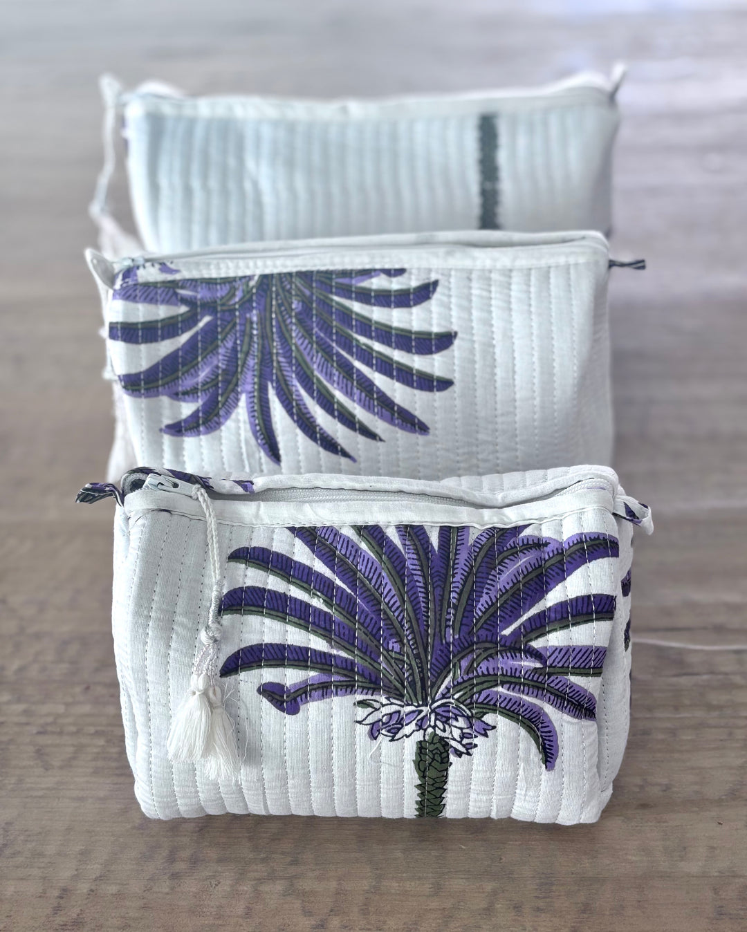 Two white pouches with purple floral designs on a wooden surface.
