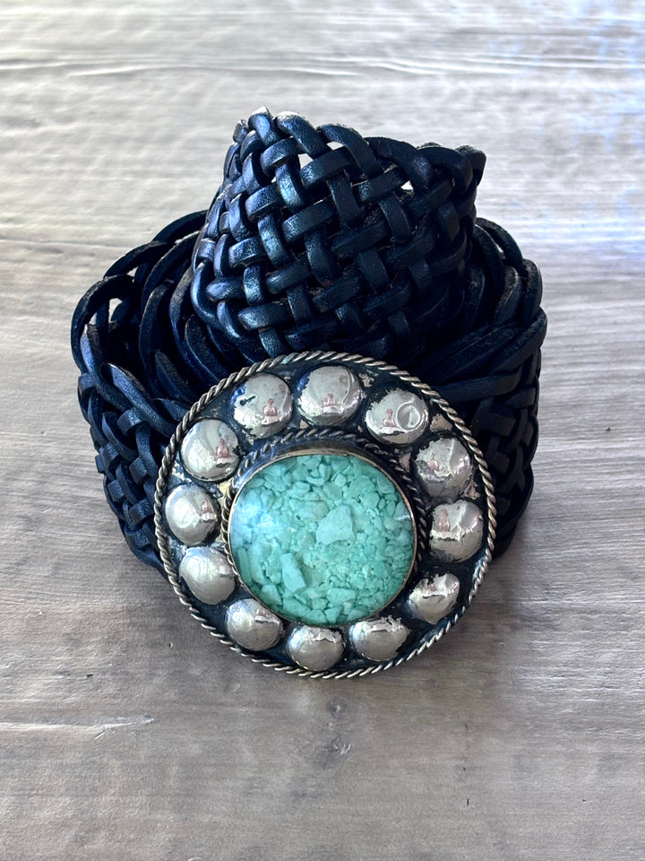 Black braided bracelet with a turquoise stone and silver accents on a wooden surface