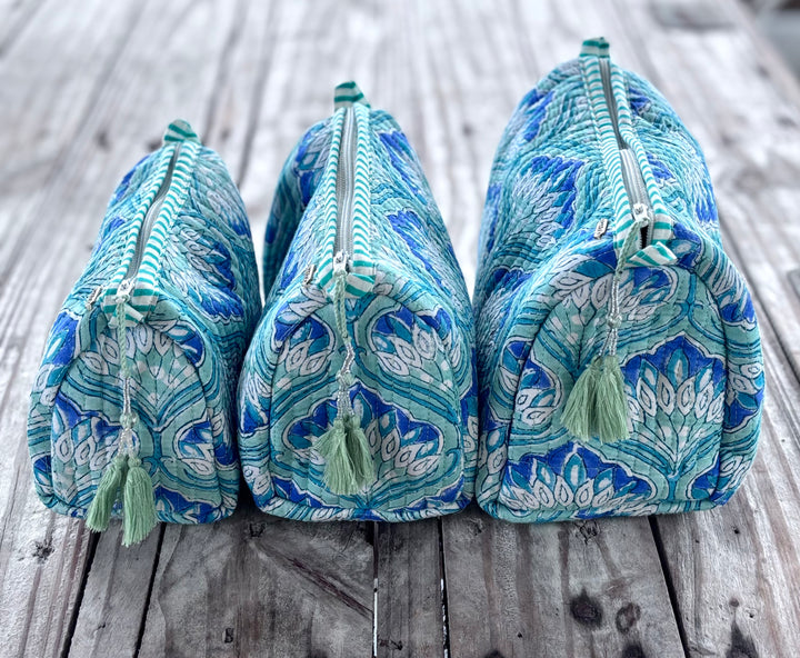 Three blue and green patterned toiletry bags with tassels on a wooden surface.