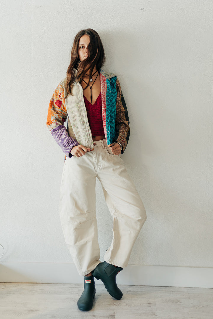 Woman wearing a colorful jacket, white pants, and green boots against a plain background