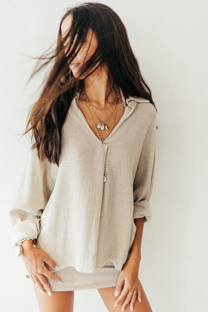 Woman wearing a beige blouse with layered necklaces against a white background