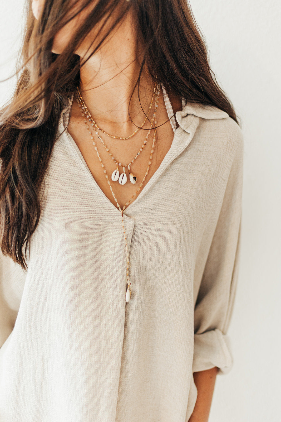Woman wearing a beige shirt and layered necklaces against a plain background