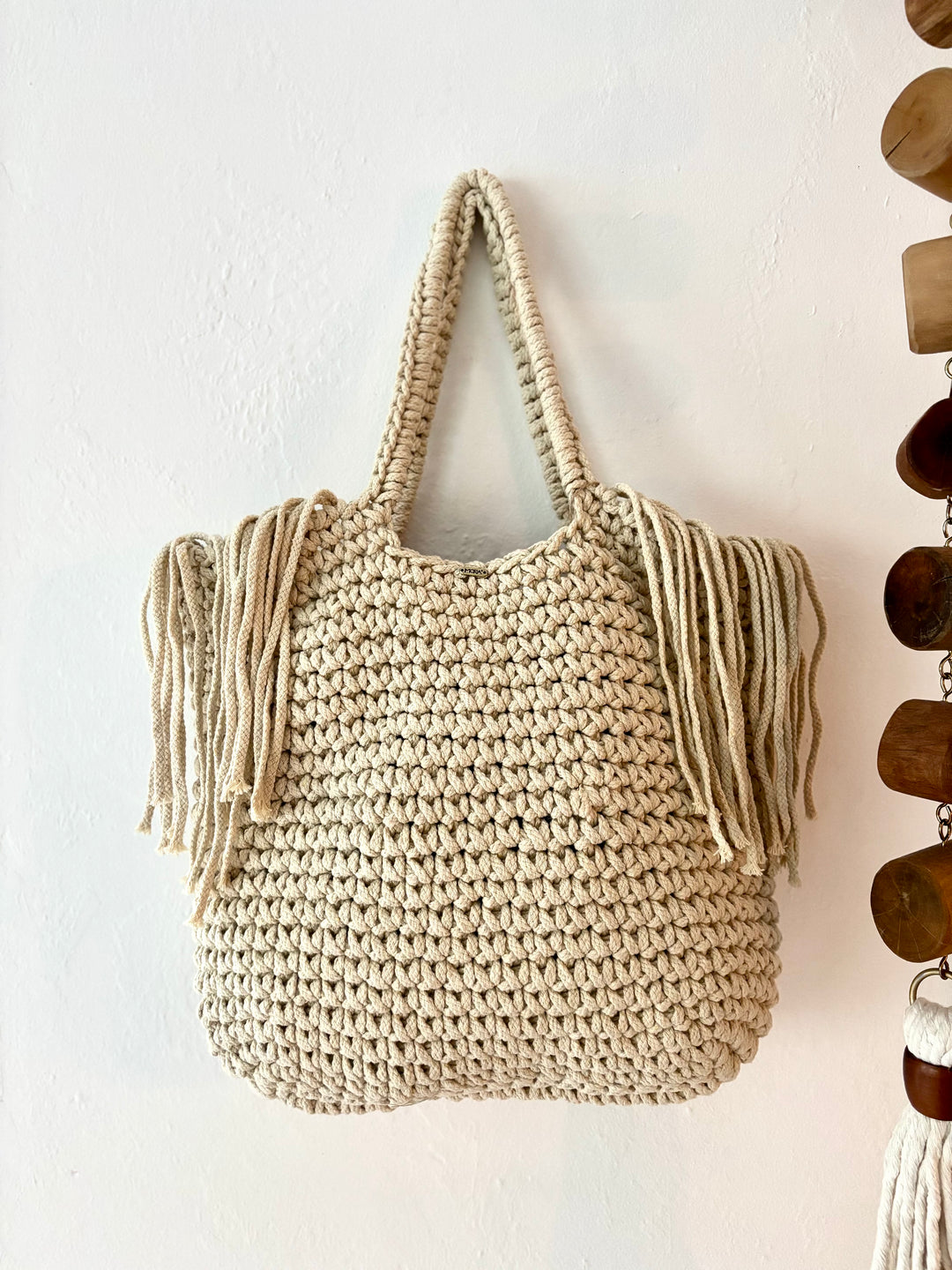 Beige woven bag with fringe on a white wall