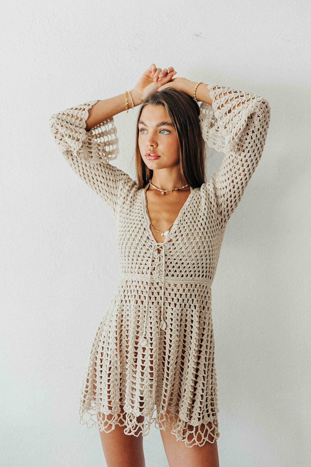 Woman wearing a beige crochet dress against a plain background