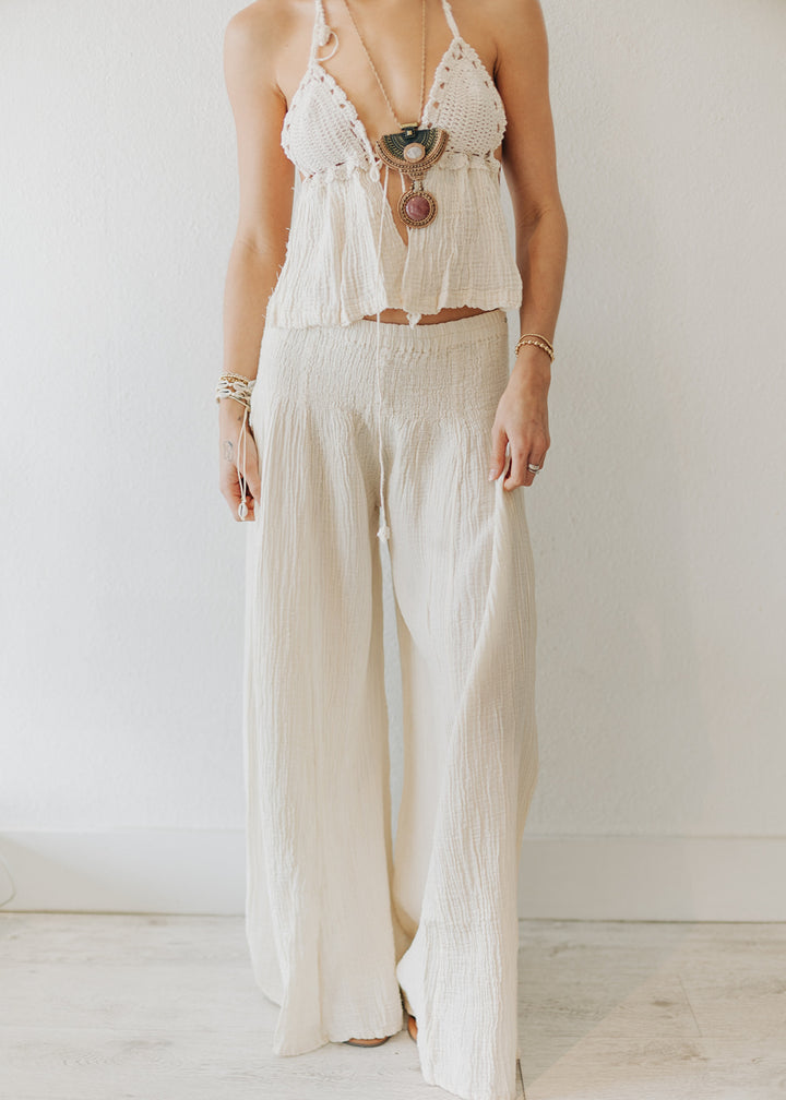 Person wearing a white crochet top and wide-leg pants against a plain background
