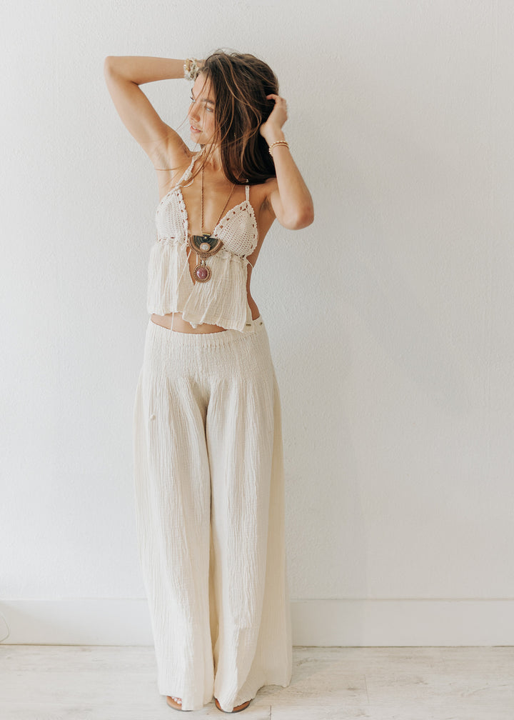 Woman wearing a white lace top and wide-leg pants against a plain background