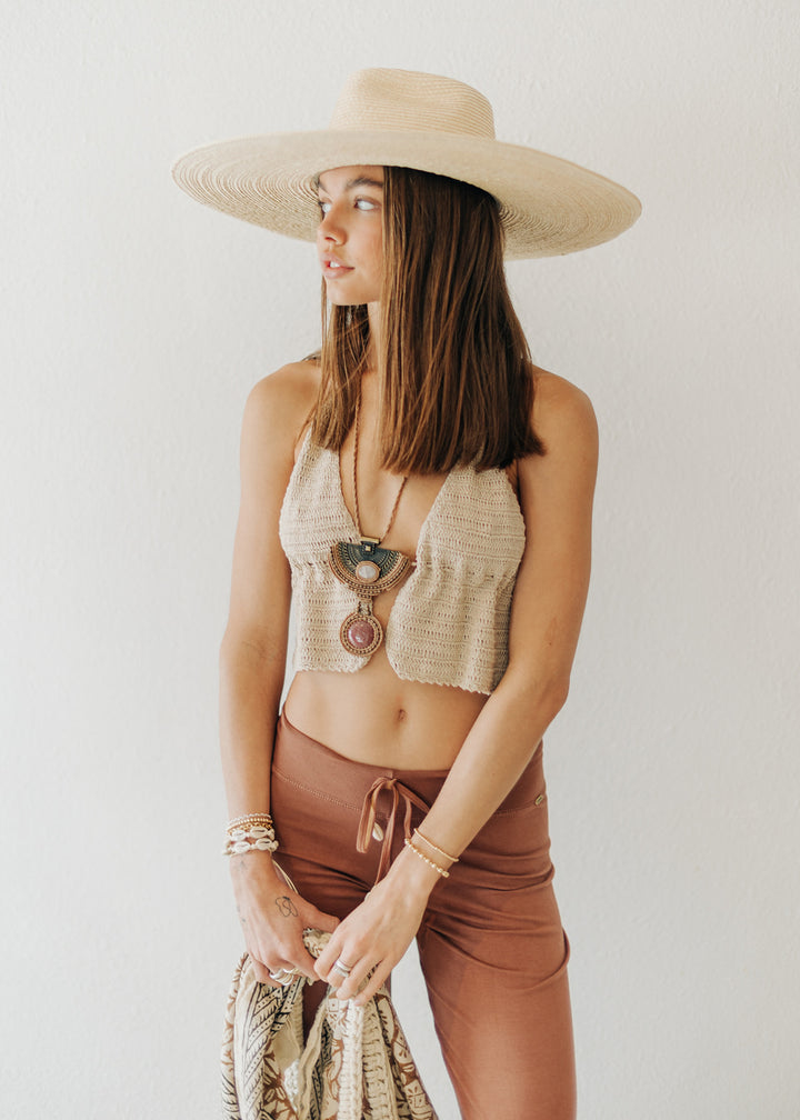 Woman wearing a beige top and brown pants with a wide-brimmed hat against a white background