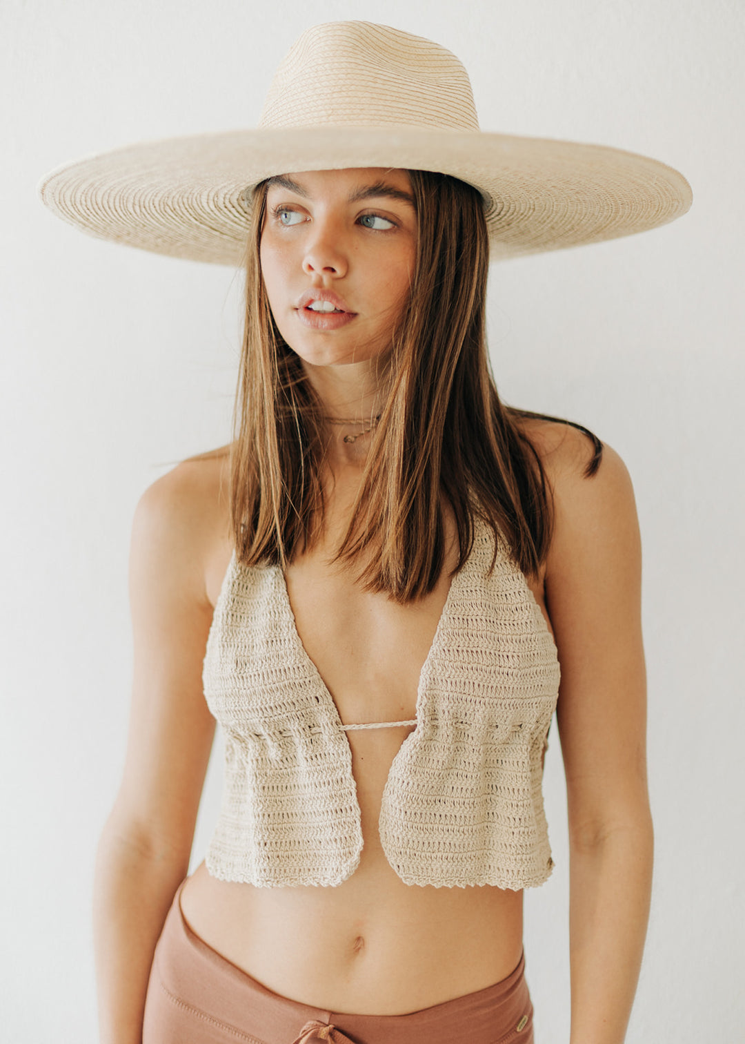 Woman wearing a wide-brimmed hat and crochet top against a white background