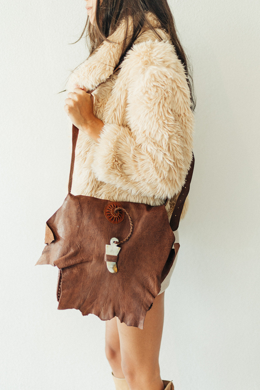 Person wearing a fur vest and brown leather skirt with a white background