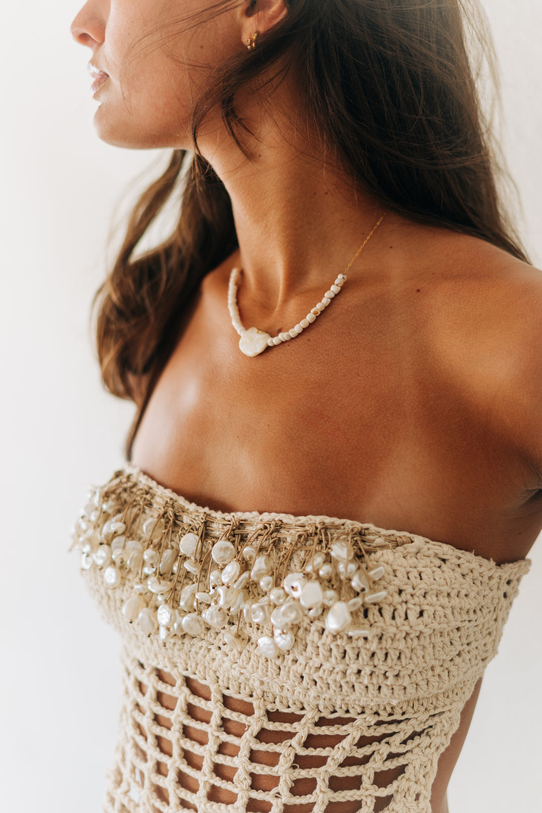 Woman wearing a beige crochet top with pearl embellishments on a white background