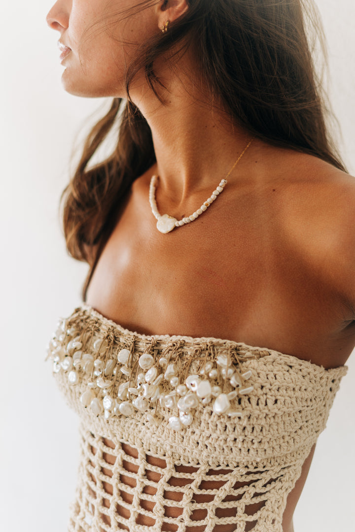 Woman wearing a beige crochet top with pearl embellishments on a white background