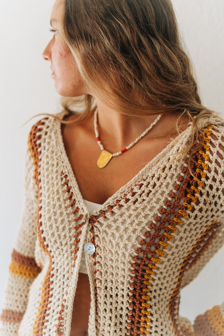 Woman wearing a beige crochet cardigan with brown and orange accents on a white background