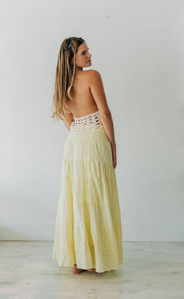 Woman in a yellow dress standing in a minimalistic room with a white wall and wooden floor.