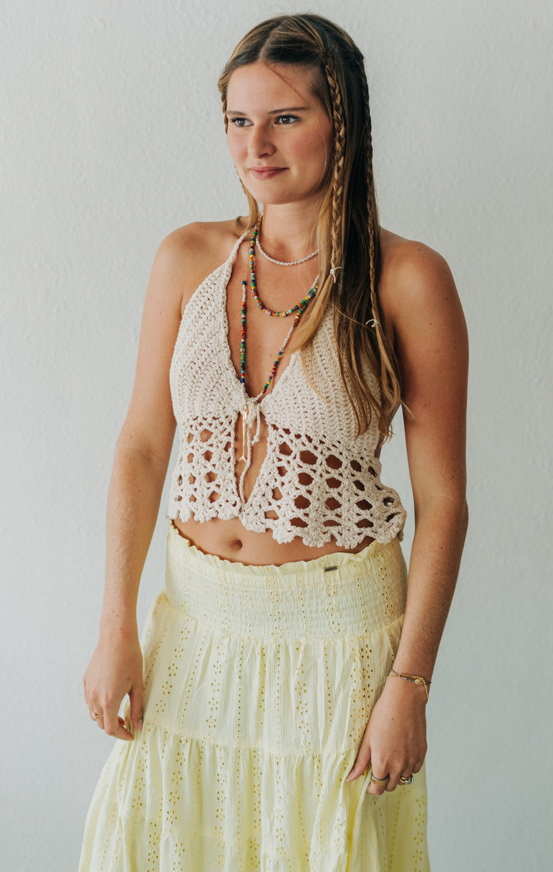 Woman wearing a crochet top and light yellow skirt against a plain background