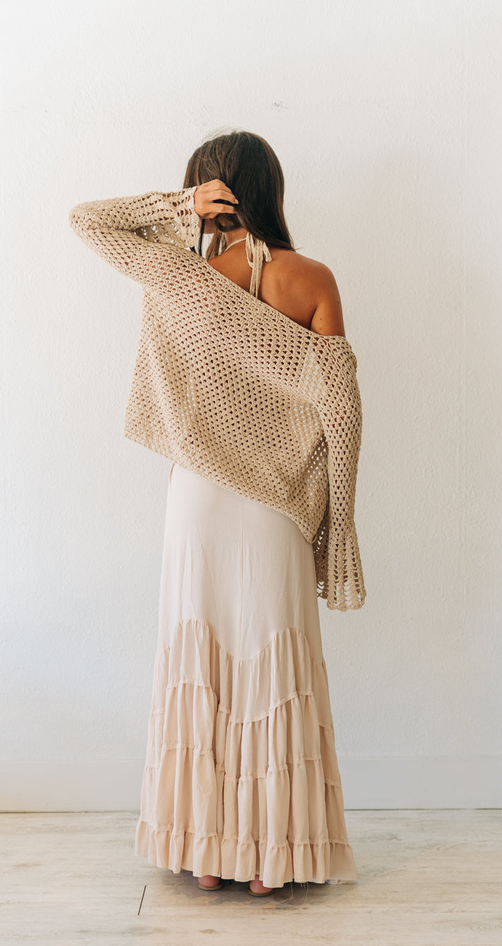 Woman wearing a beige dress with a textured shawl in a minimalistic room.