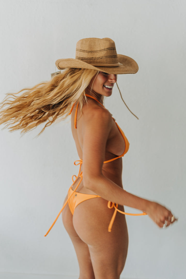 Woman wearing an orange bikini and straw hat against a plain background
