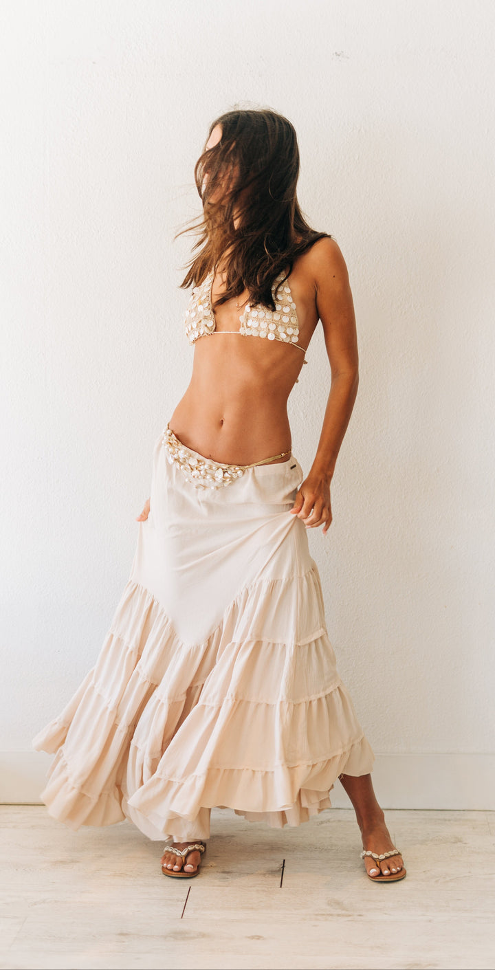 Woman wearing a white lace top and skirt against a plain white wall.