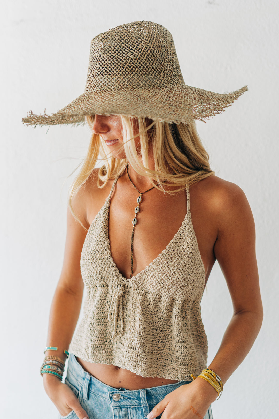 Woman wearing a straw hat and crochet top against a white background