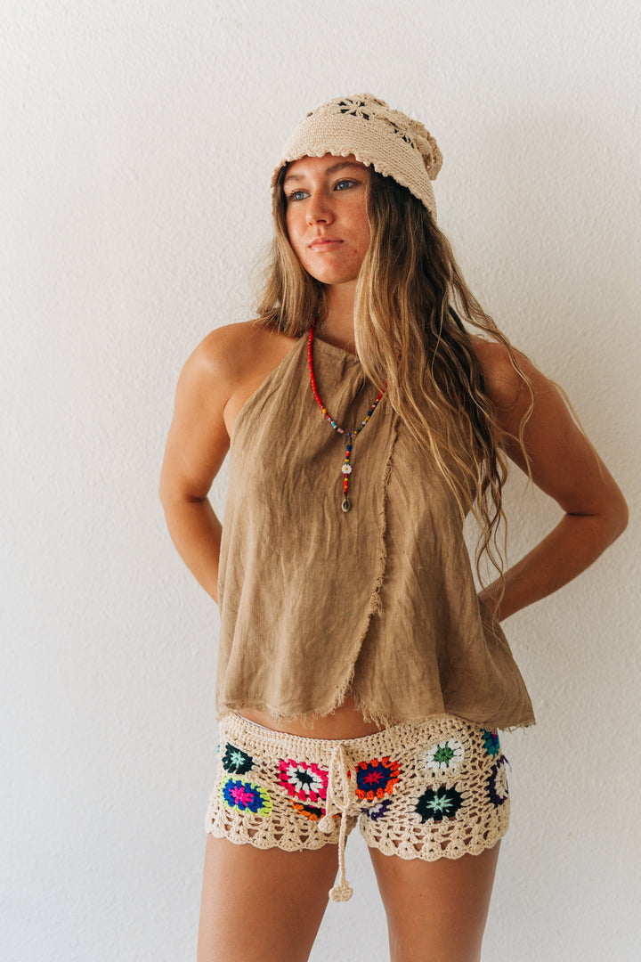 Woman wearing a beige sleeveless top and colorful crochet shorts against a white background