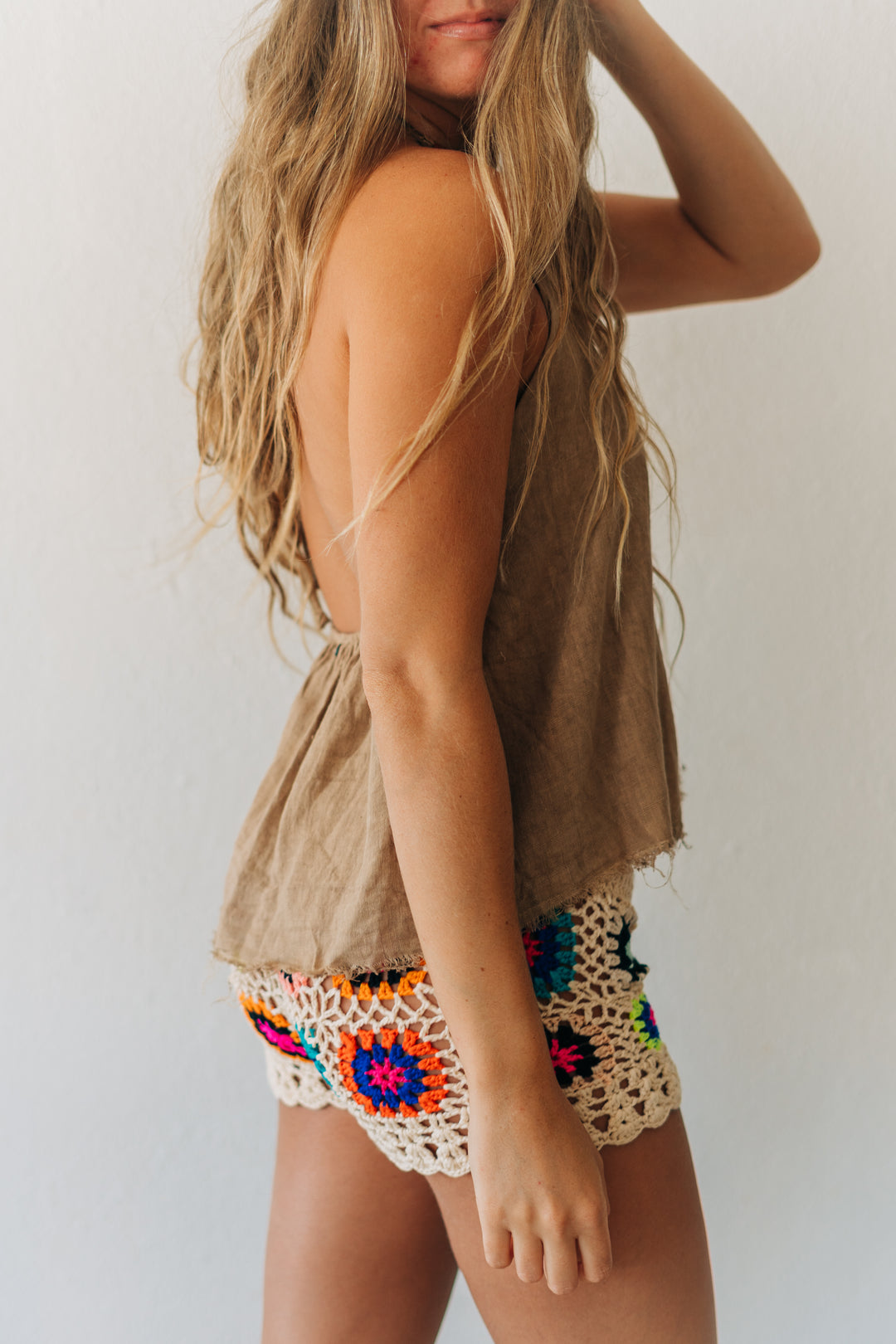 Woman wearing a beige sleeveless top and colorful crochet shorts against a white background