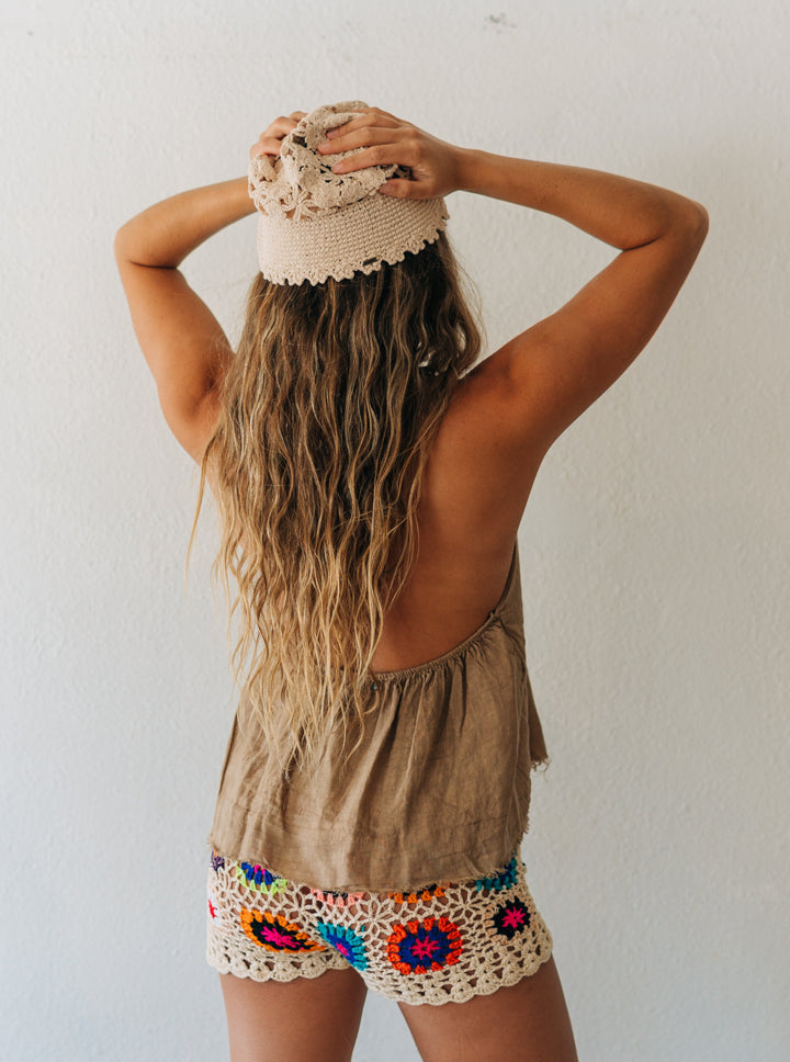 Person wearing a beige sleeveless top and colorful crochet shorts against a white wall.
