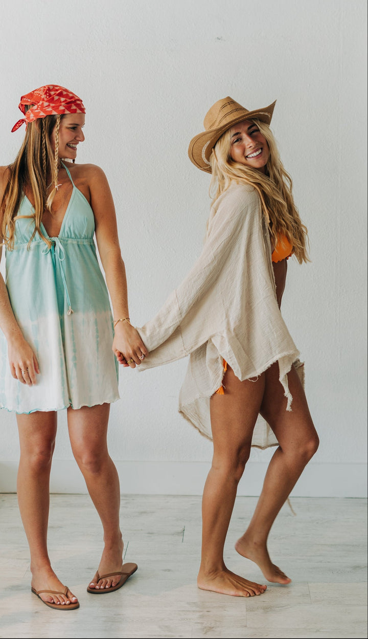 Two women holding hands in a room with a white wall and wooden floor.