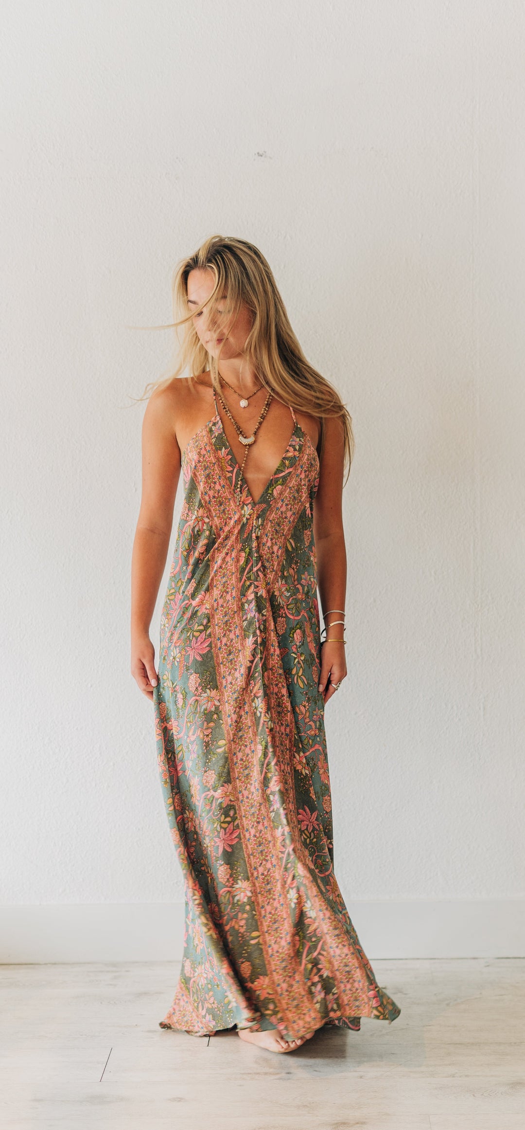 Woman wearing a floral dress standing in a room with a white wall and wooden floor.