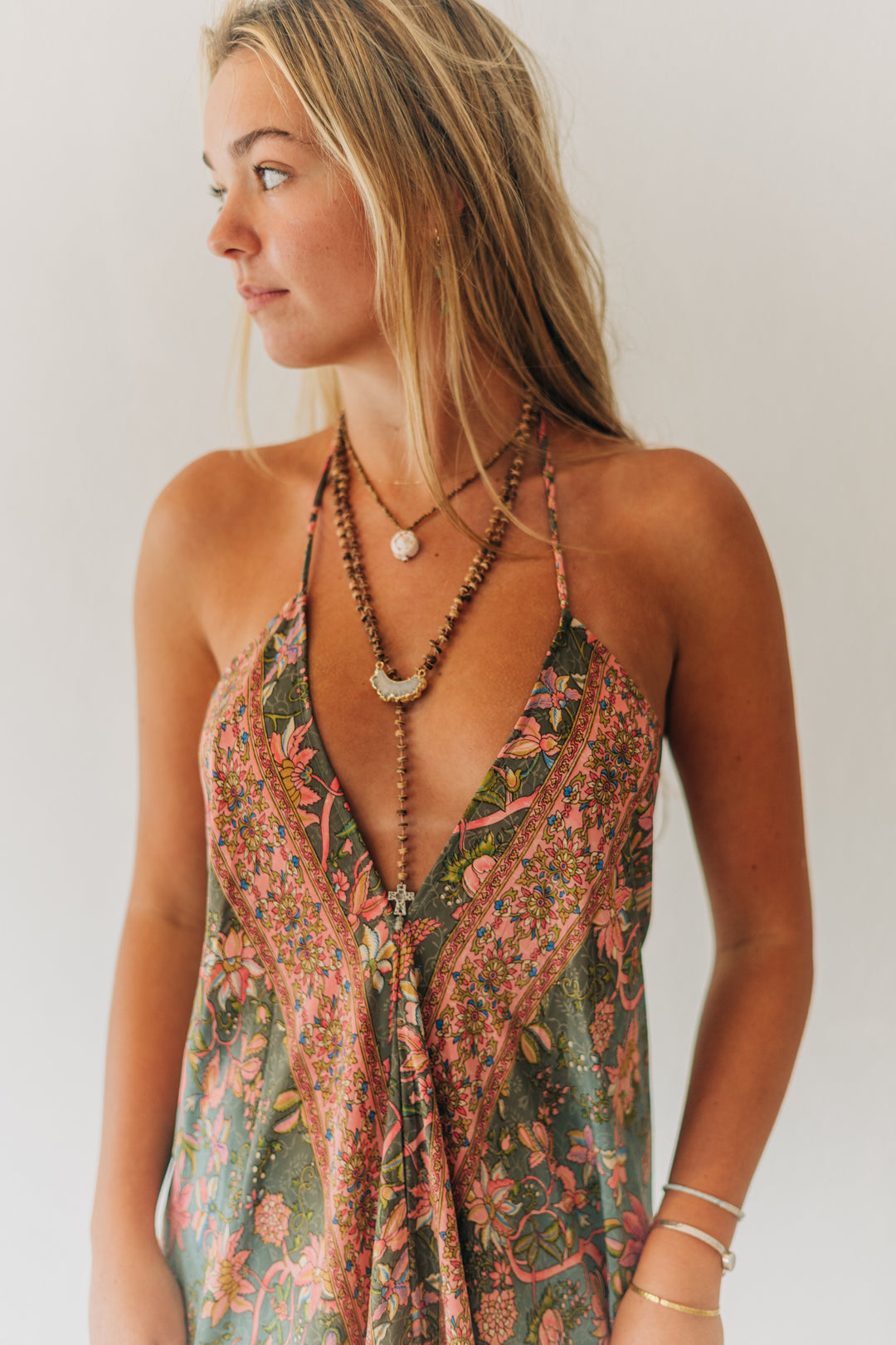 Woman wearing a floral dress with layered necklaces against a plain background