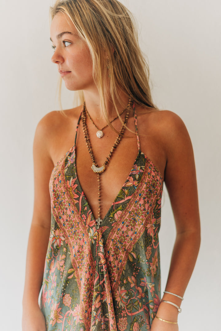 Woman wearing a floral dress with layered necklaces against a plain background