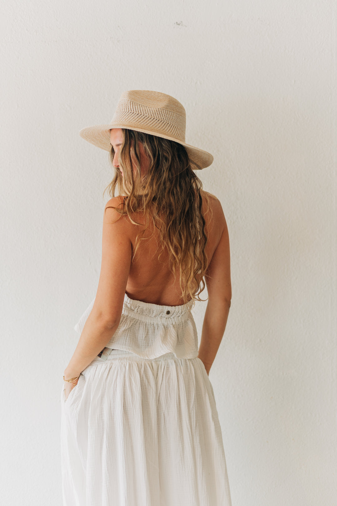 Woman wearing a tan hat, brown top, and white skirt against a plain background