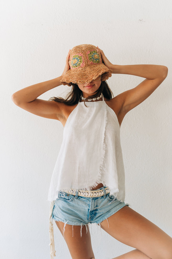 Woman wearing a straw hat with floral patterns, white top, and denim shorts against a white background