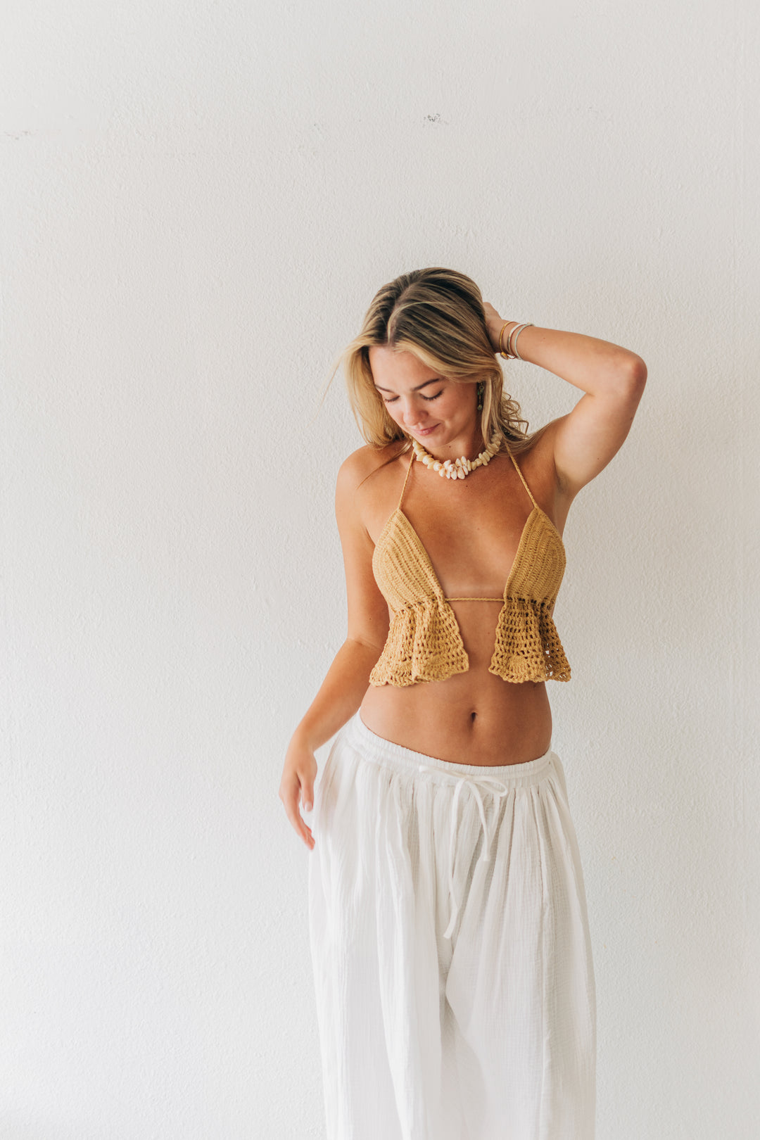 Woman wearing a yellow ruffled top and white pants against a plain background