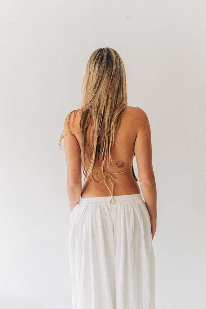 Woman with long blonde hair and a visible back tattoo wearing a white dress against a plain background