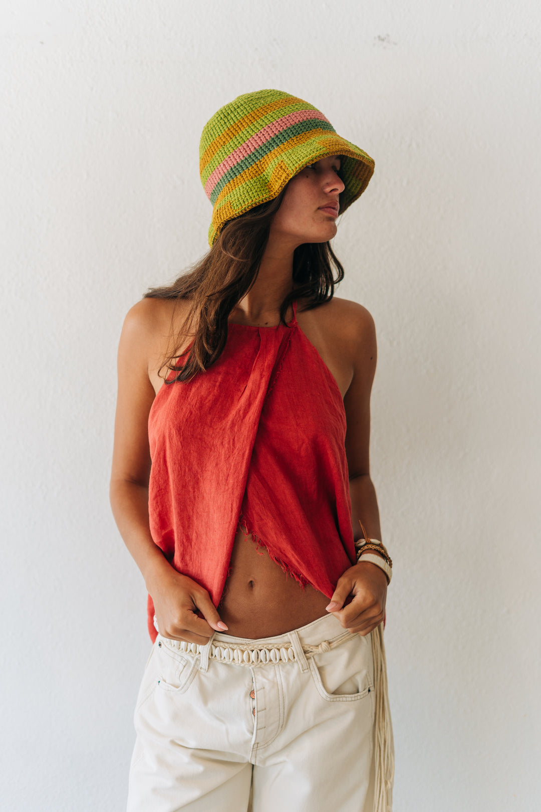 Woman wearing a colorful hat, red top, and white pants against a white background