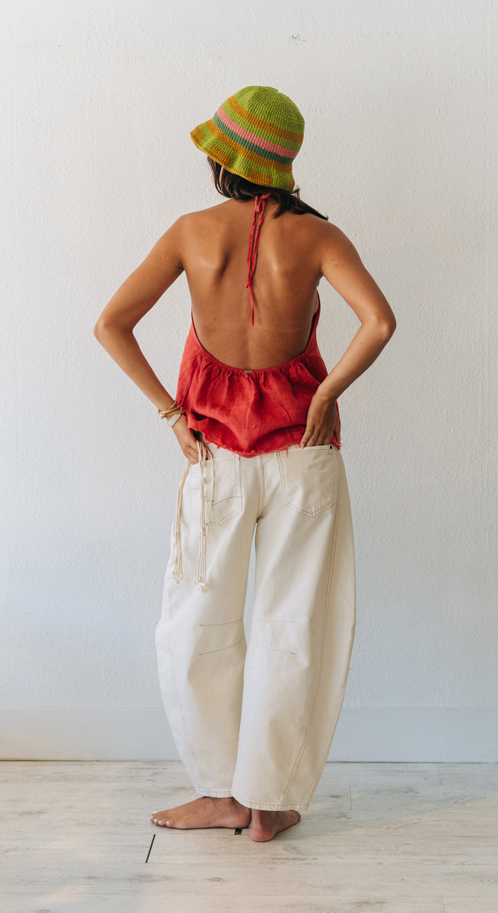 Person wearing a red top and white pants with a colorful hat, standing in a room.